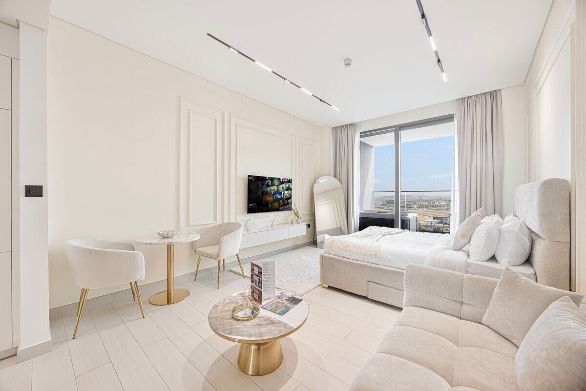 Una habitación de hotel moderna con una cama grande, una zona de estar con un sofá y sillones, una mesita redonda y un televisor.