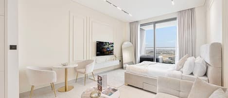 A modern hotel room with a large bed, a seating area with a sofa and chairs, a small round table, and a television.
