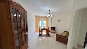 Ein geräumiges Wohnzimmer mit Holzschrank, Essbereich mit Tisch und Stühlen, einer Couch und einem Fernseher.