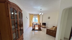 A spacious living room with a wooden cabinet, a dining area with a table and chairs, a sofa, and a television.