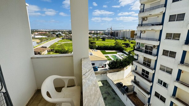 A balcony with a view of a residential area, a white chair, and a small pool area.