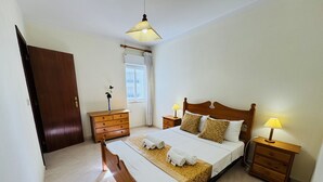 A neatly arranged bedroom with a wooden bed, bedside tables with lamps, a window with curtains, and a door.