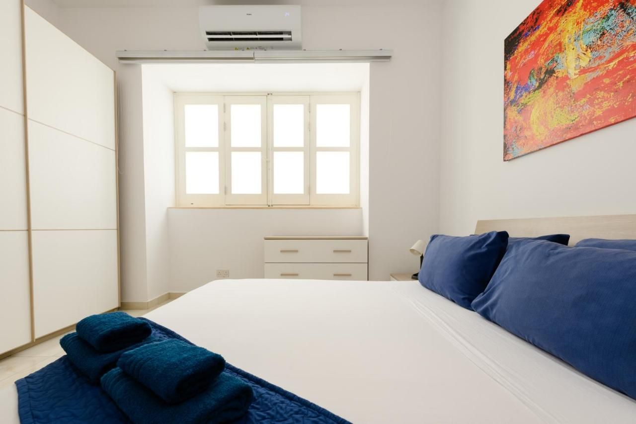 Ein Schlafzimmer mit Bett, Fenster, Nachttisch und einer Wand-Klimaanlage.