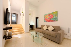 A modern living room with a glass coffee table, beige sofa, and a colorful abstract painting on the wall.
