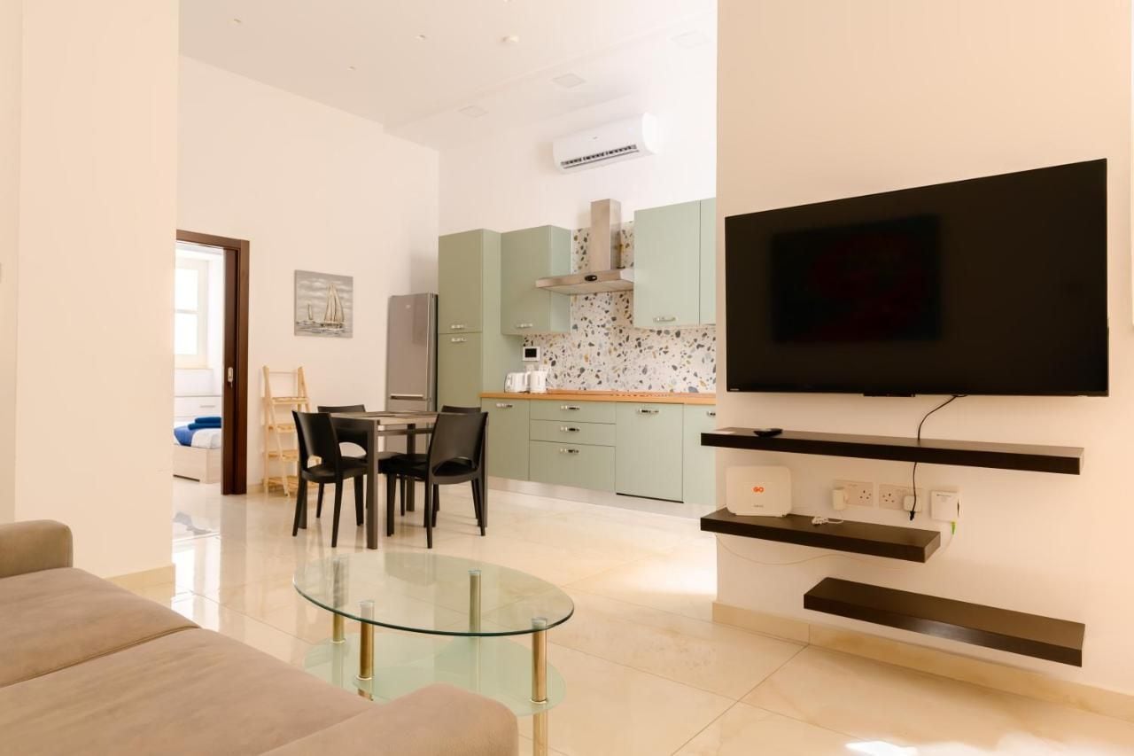 A modern living room with a glass coffee table, a flat-screen TV mounted on a wall, and a dining area with a table and chairs.
