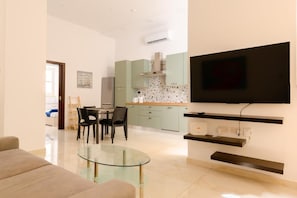 A modern living room with a glass coffee table, a flat-screen TV mounted on a wall, and a dining area with a table and chairs.