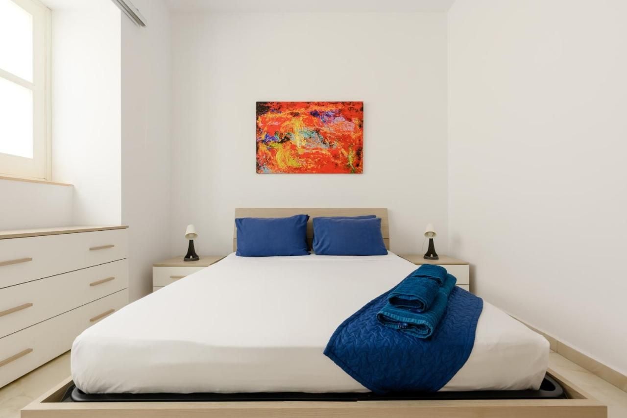 Un dormitorio con una cama, dos mesitas de noche, una ventana y un cuadro en la pared.