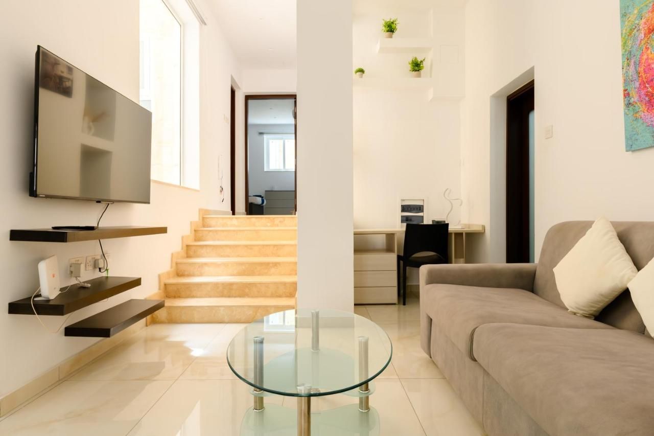 A modern living room with a flat-screen TV, a glass coffee table, a sofa, and a staircase leading to another room.