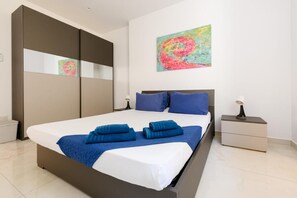 A modern bedroom with a large bed, a wardrobe, a nightstand, and a colorful abstract painting on the wall.