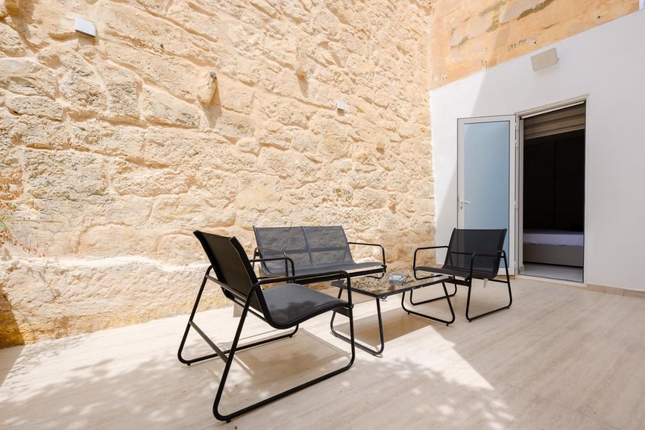 A stone wall, two black chairs, a small table, and a door leading to a room.