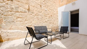 A stone wall, two black chairs, a small table, and a door leading to a room.