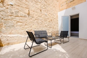 A stone wall, two black chairs, a small table, and a door leading to a room.