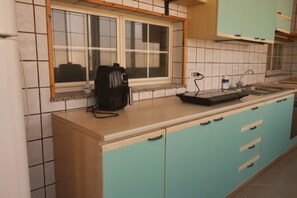 A kitchen with teal cabinets, a window above the sink, and a black appliance on the counter. - Apartment With Large Veranda Near Elmas Airport Cagliari (Elmas)