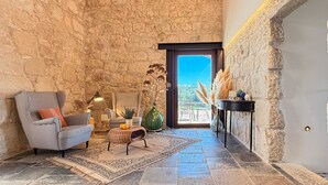 Um interior acolhedor com uma parede de pedra, uma poltrona xadrez, uma mesa pequena com abajur e vista através de uma porta.