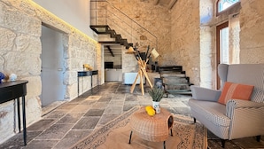 Interior com paredes de pedra, uma escada, uma cadeira de vime e uma mesa com um vaso.