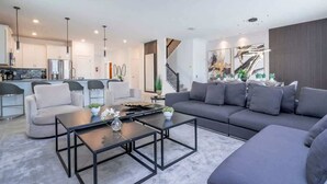 Ein modernes Wohnzimmer mit einem grauen Sofa, einem Couchtisch und einer Küche im Hintergrund.