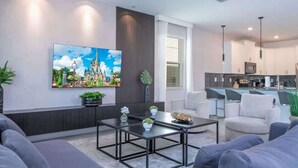 Ein modernes Wohnzimmer mit einem großen Flachbildfernseher, einem Couchtisch und grauen Sofas.