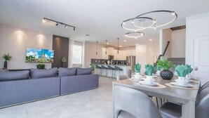 Ein modernes Wohnzimmer mit grauem Sofa, einer Essecke mit Tisch für zwei Personen und einer Küche im Hintergrund.