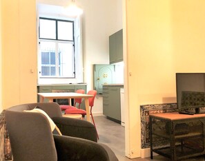 Una habitación con una mesa de comedor y sillas, un televisor y una zona de cocina con armarios y una ventana.