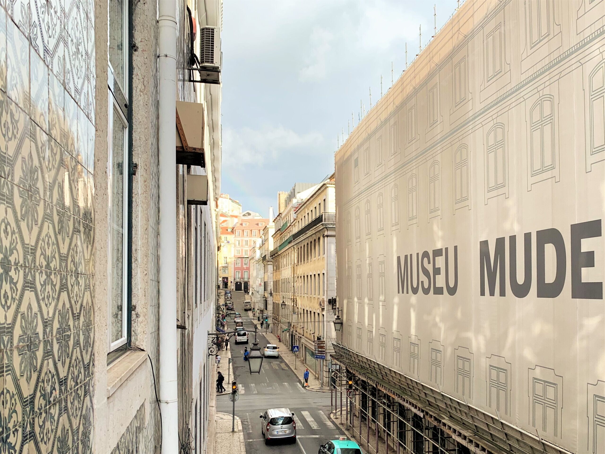 Vista de la calle con un edificio que dice "MUSEU MUDE" y una pared de azulejos a la izquierda.