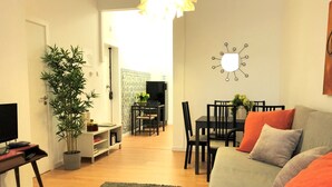 A living room with a sofa, a TV, a dining table, chairs, a potted plant, and a wall clock. - SJ1E + SJ1D Spacious & Comfortable | 2 Apts | A/C (Lisboa ciudad)