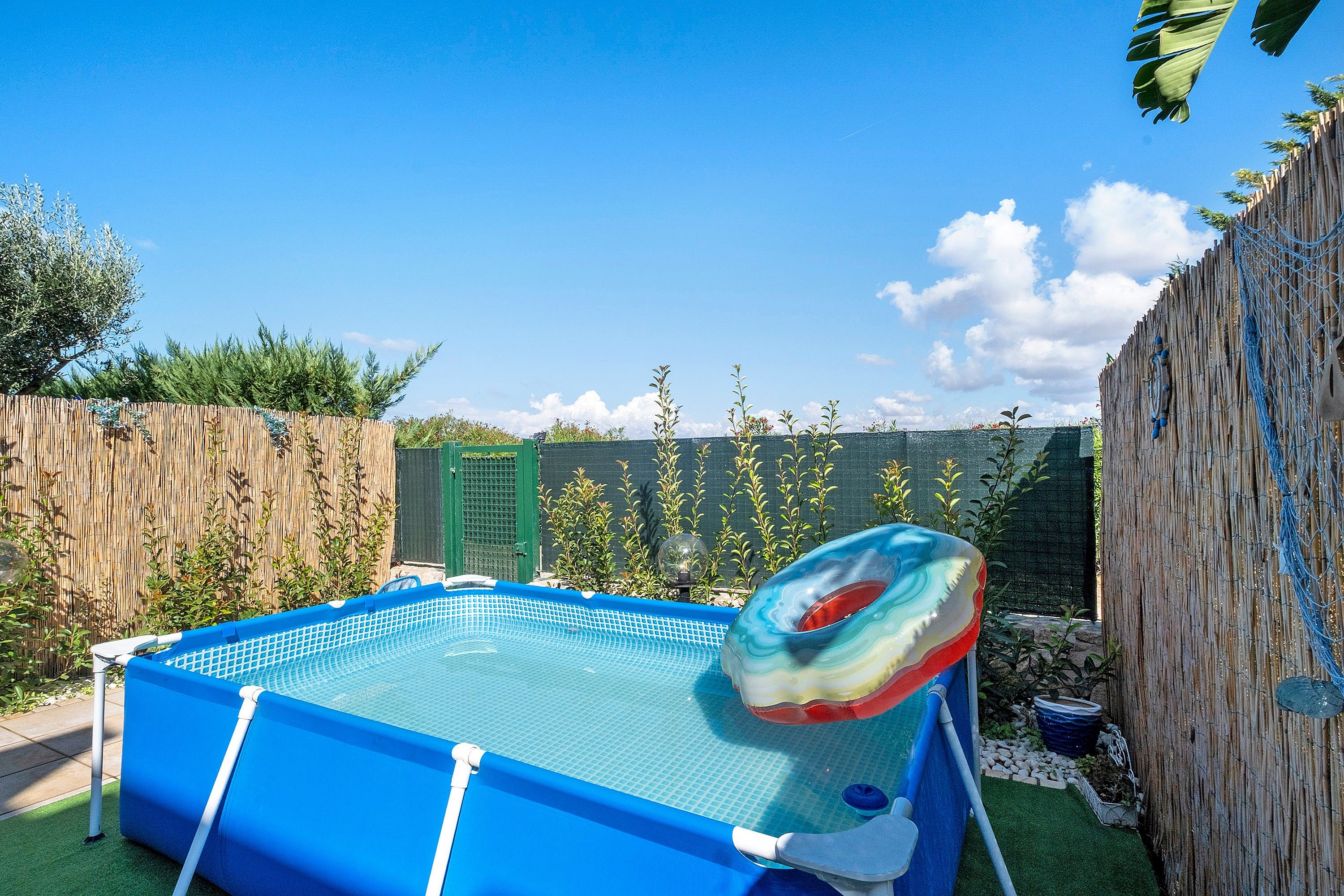 Ein aufblasbarer Pool mit einem bunten Ring-Schwimmpfad, umgeben von einem Holenzaun und Grünpflanzen.
