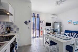 Een moderne keuken met witte kasten, een eettafel met blauwe kussens en een aan de muur bevestigde televisie.