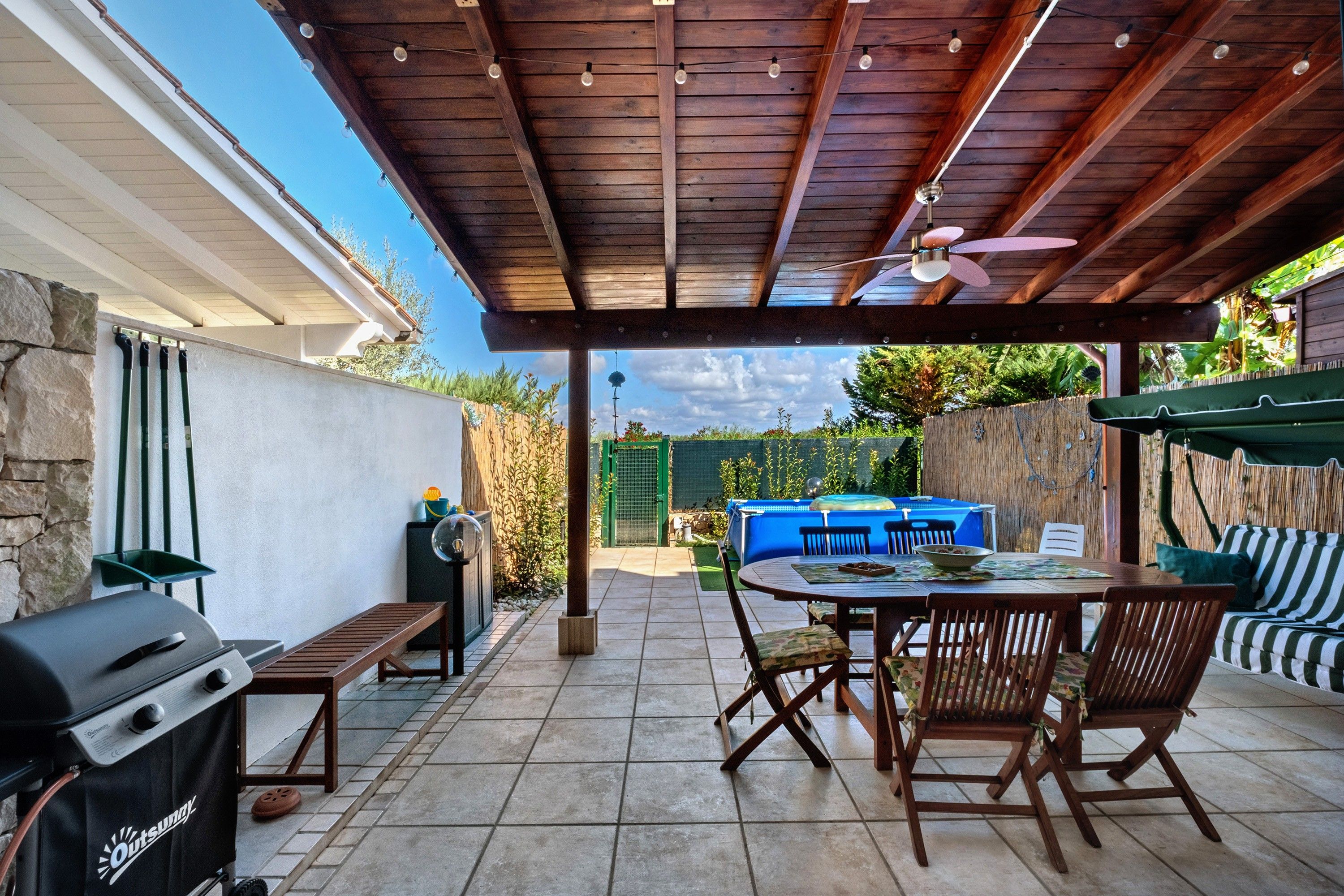 A covered patio with a grill, seating area, and a view of the backyard.
