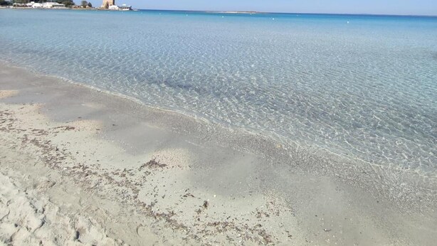 A beach with clear water, a sandy shore, and a building in the distance.