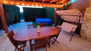 An outdoor patio with a wooden table and chairs, a swing, and a covered seating area.