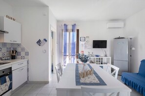 Een moderne keuken met witte kasten, een eethoek met een witte tafel en stoelen, en een blauwe bank.