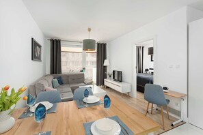 Ein modernes Wohnzimmer mit Essbereich, einer Couch, einem Fernseher und einem Esstisch, gedeckt mit Tellern und Gläsern.