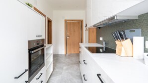Eine moderne Küche mit weißen Schränken, einem eingebauten Ofen, einer Edelstahl-Dunstabzugshaube und einem Messerblock auf der Arbeitsplatte.