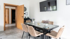 Ein moderner Essbereich mit einem Glastisch, vier gepolsterten Stühlen, einem an der Wand befestigten Flachbildfernseher und einer Holztür, die in einen anderen Raum führt.
