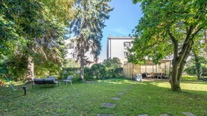Un jardín con un camino pavimentado, asientos exteriores y un edificio al fondo.