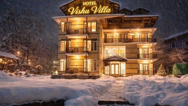 Ein mehrstöckiges Hotel namens 'Vishu Villa' mit einer auffälligen beleuchteten Signatur, einem überdachten Eingang und einer verschneiten Landschaft.