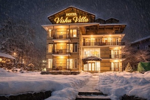 A multi-story hotel named 'Vishu Villa' with a prominent illuminated sign, a covered entrance, and a snow-covered landscape. - The Turg Resort (Manali)