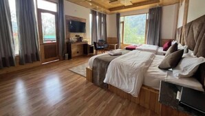 Ein Hotelzimmer mit Holzboden, einem Bett mit weißer Bettwäsche, einem Schreibtisch mit Stuhl und einem an der Wand montierten Fernseher.