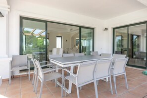 Um pátio espaçoso com mesa e cadeiras, grandes portas de correr de vidro e vista para o exterior.