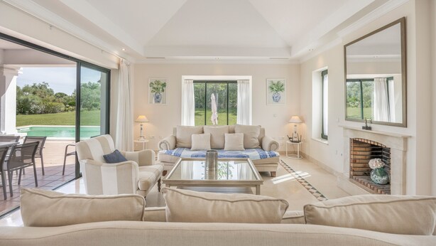 A spacious living room with a large sofa, a coffee table, and a fireplace. There are large windows providing a view of the outdoors. - Villa 'Arcos Golf Jacaranda 11' with Mountain View, Wi-Fi and Air Conditioning (Arcos de la Frontera)