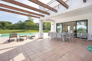 Un patio techado con piscina, mobiliario exterior y vistas al follaje.