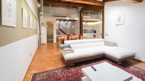A modern living room with a sectional sofa, a coffee table, and a kitchen in the background. - Alkimia Apartments (Ferrara)