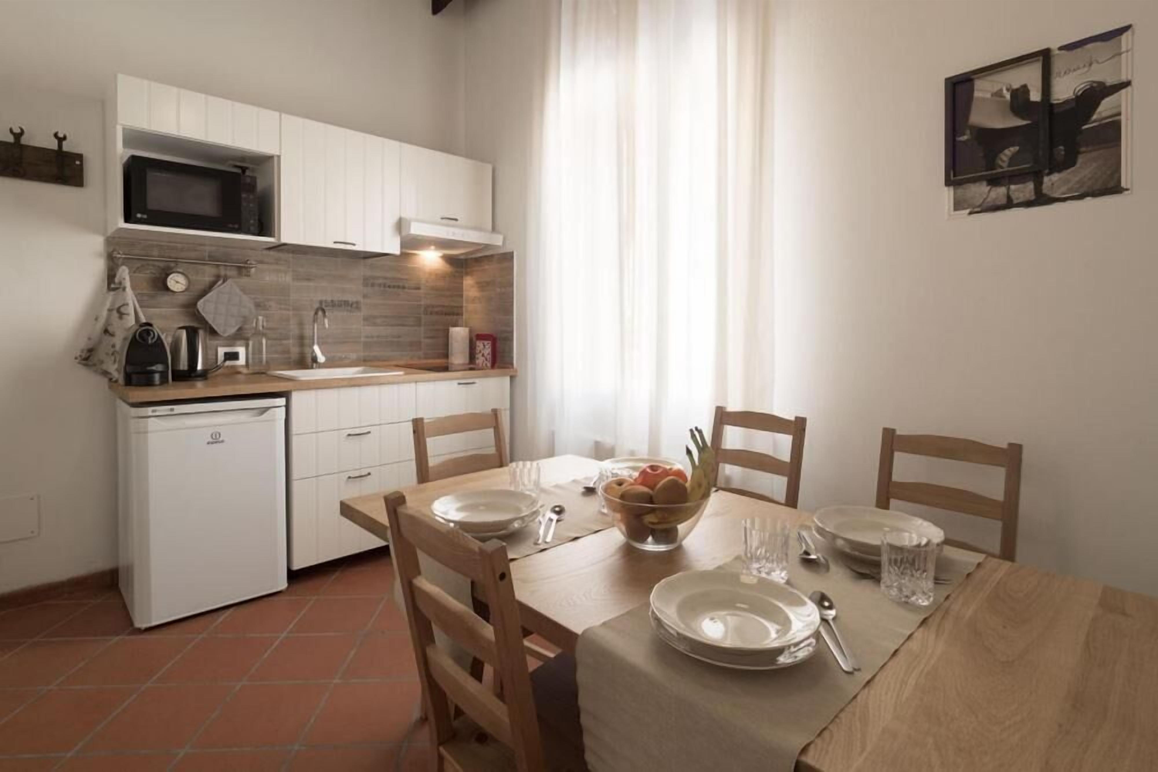 A compact kitchen with white cabinets, a microwave, and a sink. There is a dining table with chairs and a bowl of fruit.