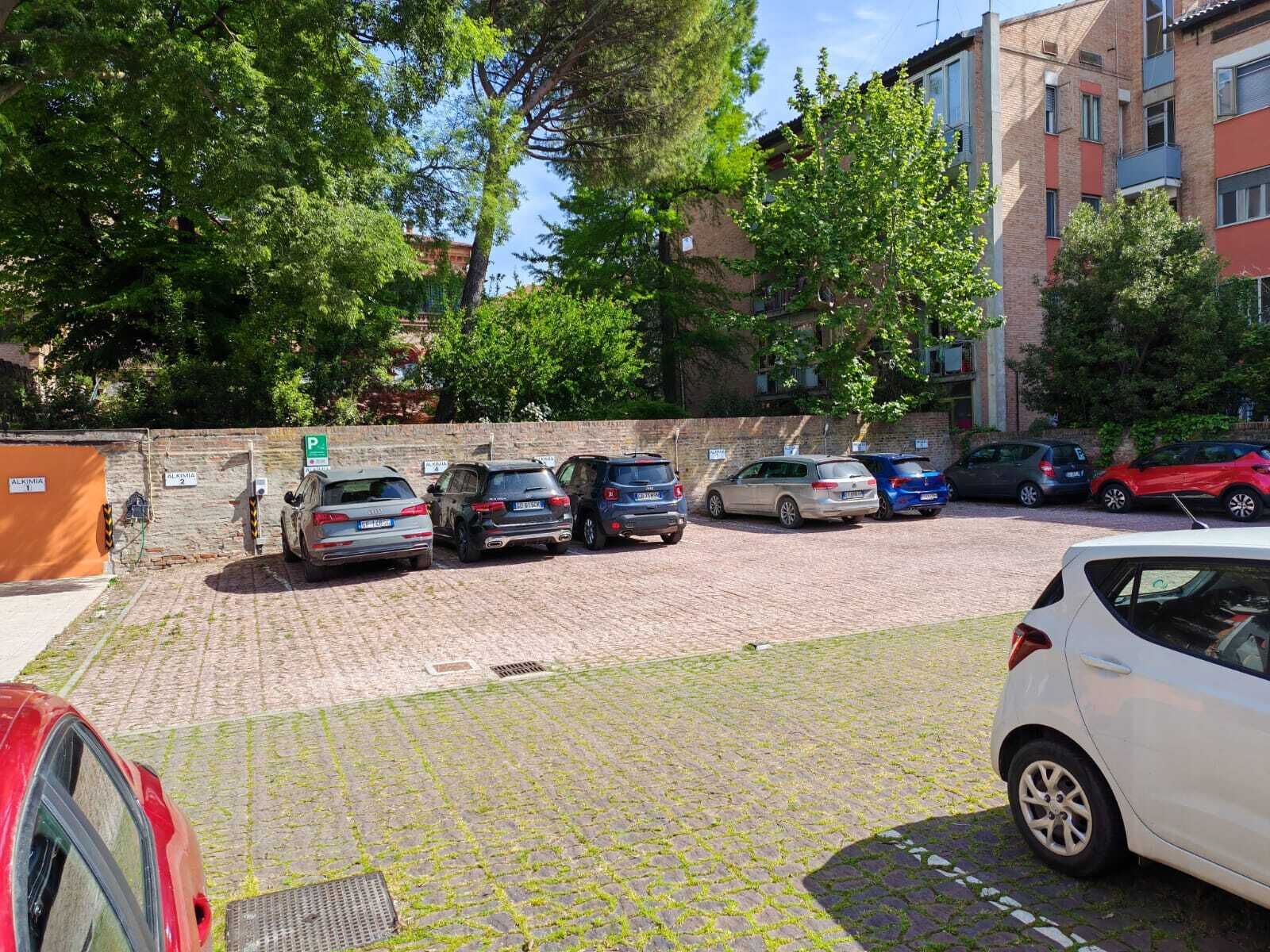 A parking area with multiple cars, a brick wall, and a building with balconies in the background.