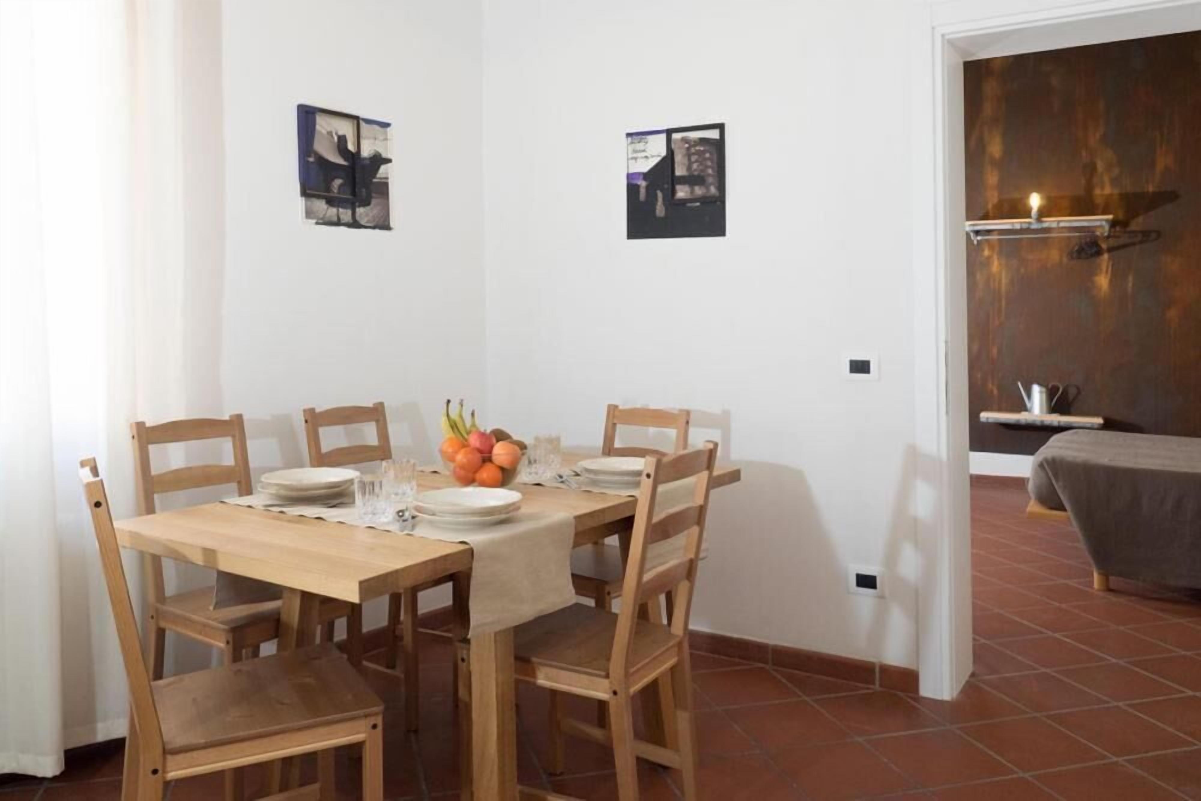 Un comedor con una mesa de madera dispuesta para cuatro, rodeada de sillas de madera. Hay dos cuadros enmarcados en la pared sobre la mesa.