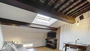 A spacious loft with a high ceiling, wooden beams, a skylight, a sofa, a dining table, and a fireplace. - Alkimia Apartments (Ferrara)