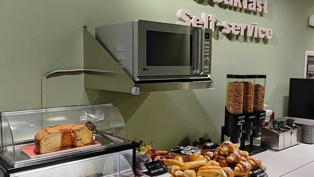 A breakfast self-service station with a variety of pastries, a display case with cakes, and a microwave. - Alkimia Apartments (Ferrara)