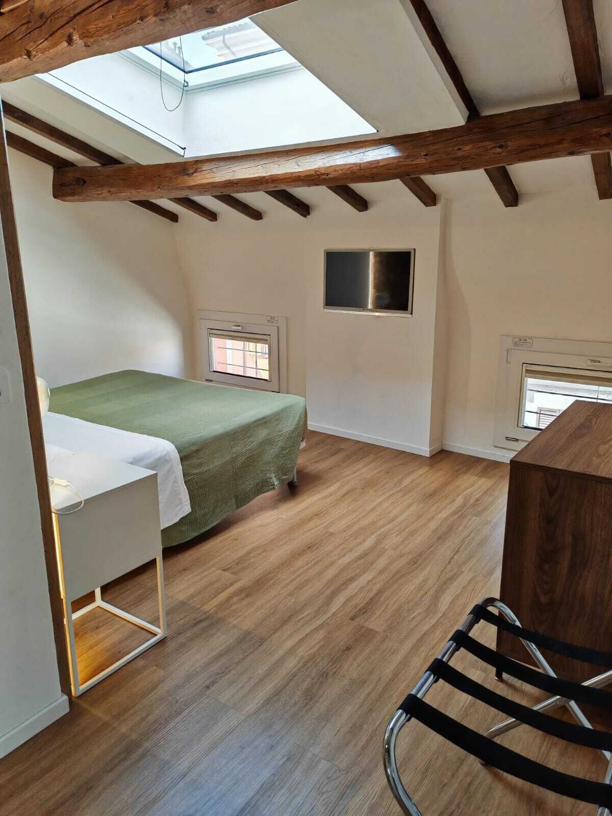 Een kleine, open ruimte met een hoge kap, houten balken, een bed, een bureau en een stoel.