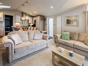 A modern living room with a beige sofa, a wooden coffee table, and a dining area with a kitchen in the background. - Lighthouse View by Interhome (Lossiemouth)