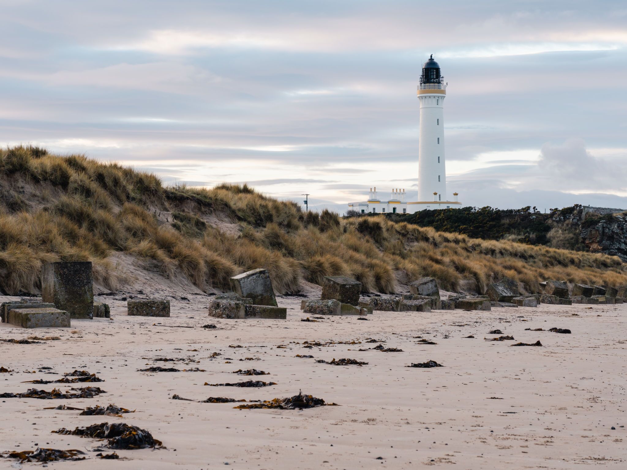 A lighthouse on a sandy beach with grassy dunes in the background.